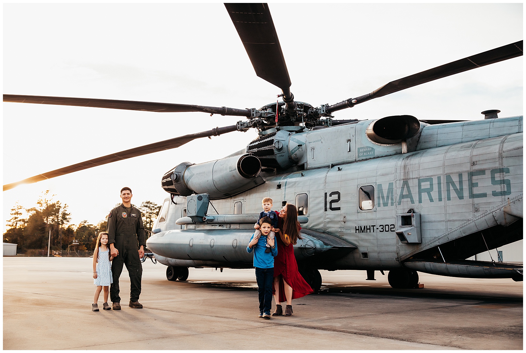 Marine family posing on flight line with a ch-53 helicopter in the back