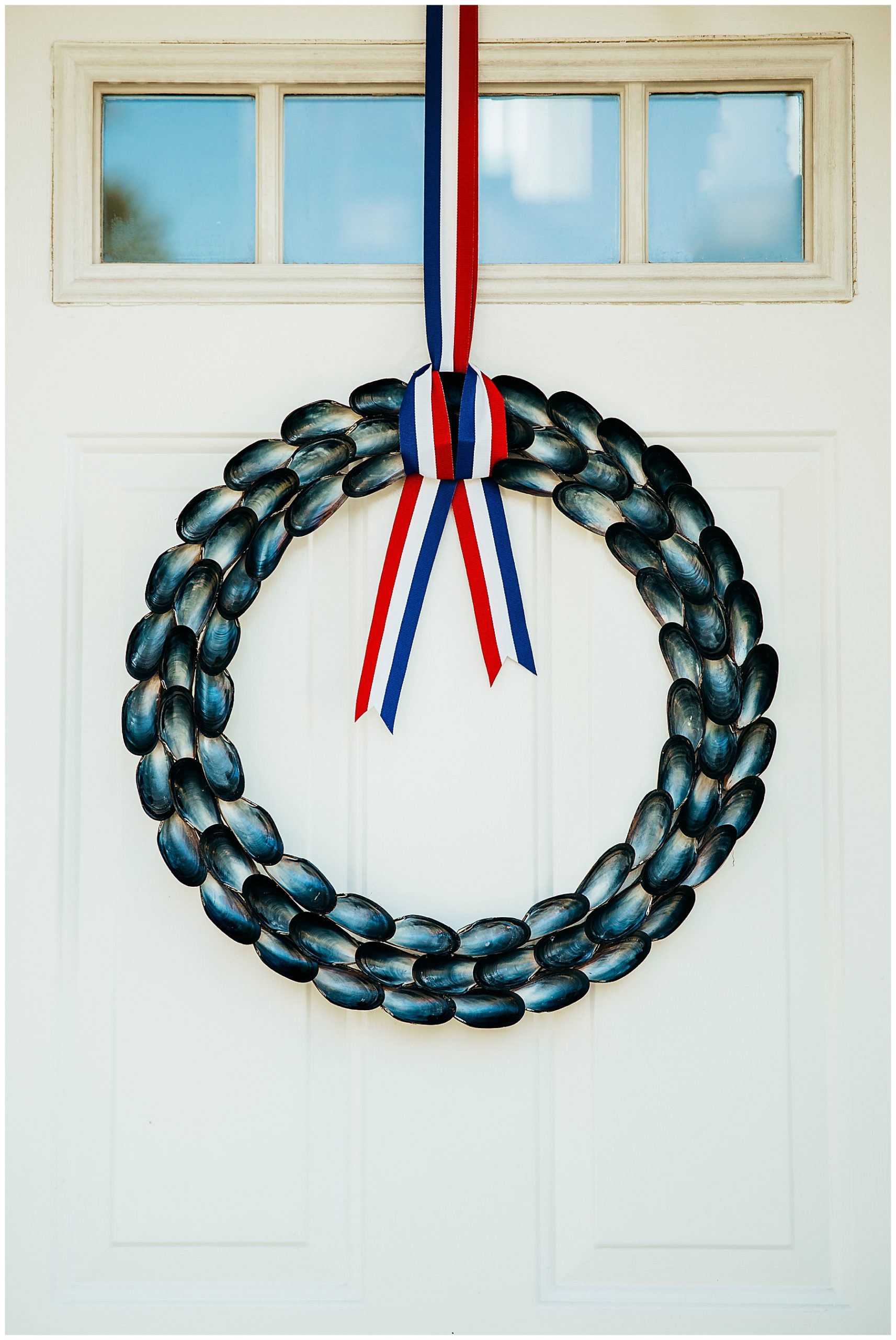 Mussel shell wreath with red white and blue ribbon hung on front door