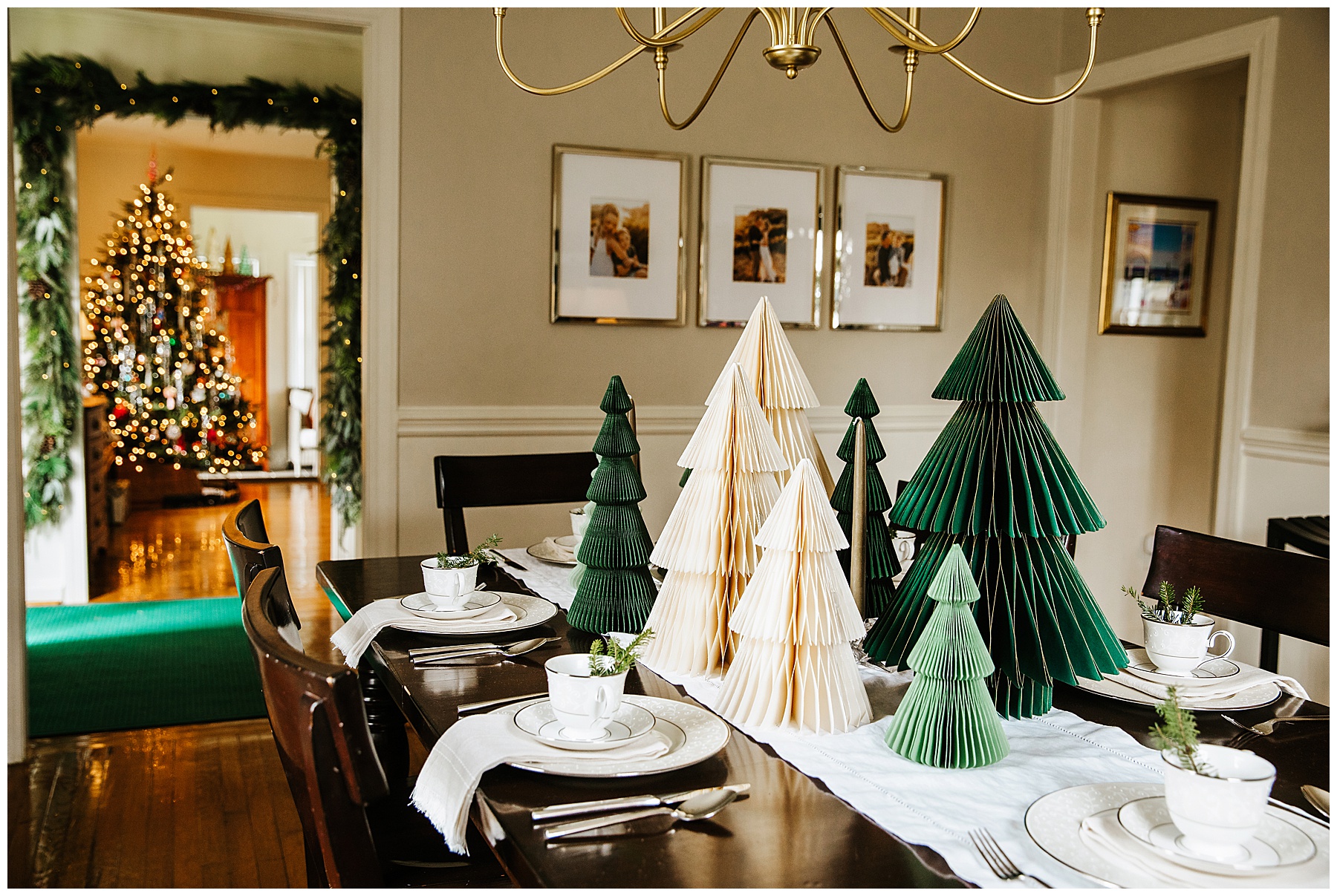 Dining room table decorated with paper Christmas trees showing the family Christmas tree in the distant room.